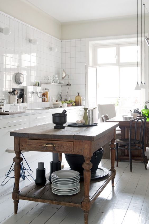 a white Scandinavian kitchen with white square tiles on the walls, a vintage stained kitchen island and a table in one, pendant lamps