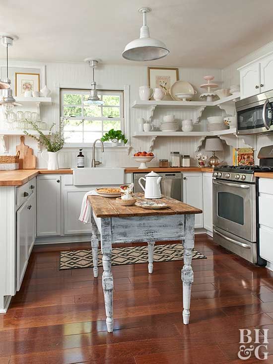 a white cottage kitchen with shaker style cabinets, butcherblock countertops, a shabby chic dining table that doubles as a kitchen island