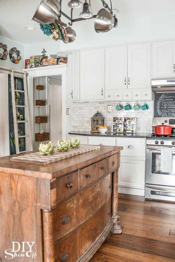a white farmhouse kitchen with a marble tile backsplash, a vintage kitchen island that is a buffet, pretty artworks