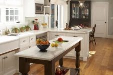 a white farmhouse kitchen with shaker style cabinets, a dark vintage kitchen island, vintage glass pendant lamps and potted plants