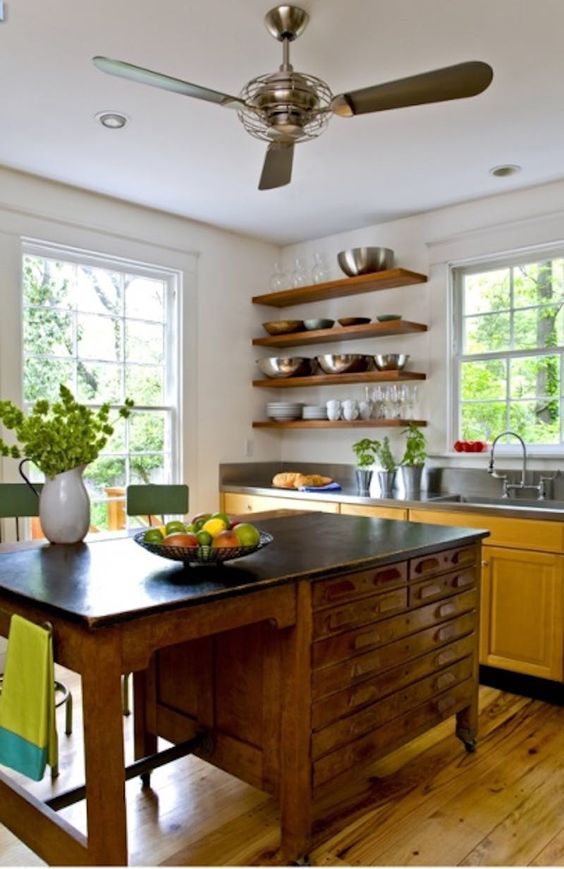a yellow kitchen with dark countertops, open shelves instead of upper cabinets, a vintage desk as a kitchen island and green stools
