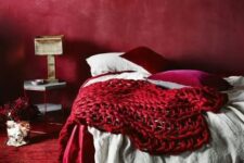 an all-red bedroom with a red wall, carpet, pillows and a chunky knit blanket for a passionate look