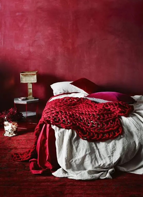 an all-red bedroom with a red wall, carpet, pillows and a chunky knit blanket for a passionate look