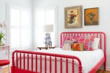 an artistic bedroom with a bold red vintage bed and a stool, chic artworks, a table lamp with elephants and a vintage chandelier