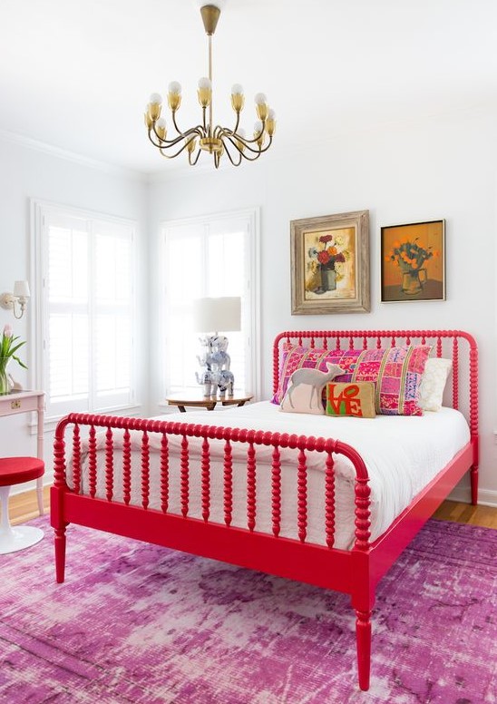 an artistic bedroom with a bold red vintage bed and a stool, chic artworks, a table lamp with elephants and a vintage chandelier