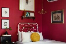 an eclectic guest bedroom with bold red walls, a vintage metal bed, a black nightstand and a gallery wall with vintage artworks
