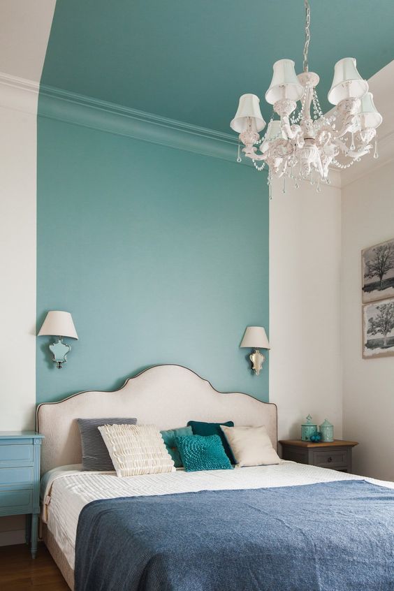 an elegant bedroom with a turquoise stripe on the wall and ceiling, a refined upholstered bed with colorful bedding, mismatching nightstands and a chic chandelier