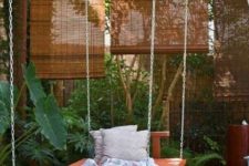 an outdoor hanging bed on chains with bright bedding, blankets and pillows is a fit for a tropical space