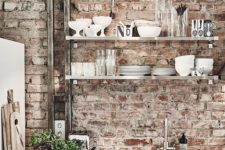 white and shiny metal kitchen cabinets and red brick walls that make the space look more distressed and relaxed