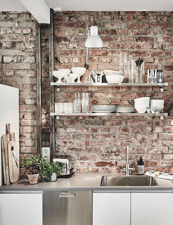 white and shiny metal kitchen cabinets and red brick walls that make the space look more distressed and relaxed