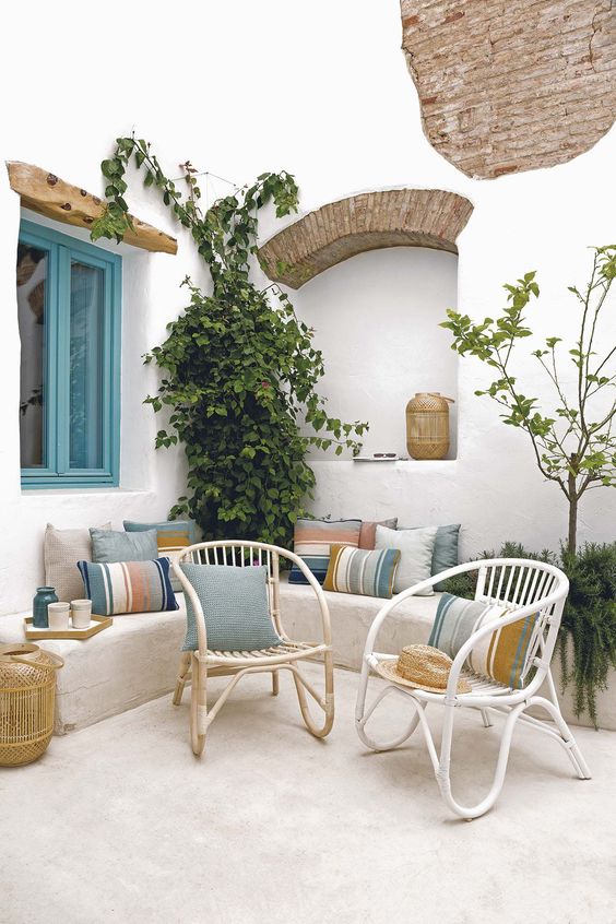 a Mediterranean beach patio with wicker furniture, bright pillows, potted plant and woven candle lanterns