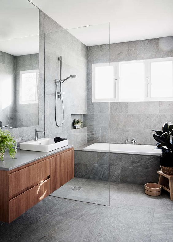 a bathroom done with grey marble tiles a floating vanity, a seamless glass shower door