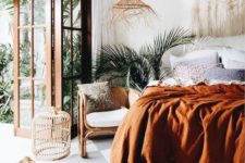 a boho tropical bedroom with a macrame wall hanging, a wicker pendant lamp, muted colored bedding and rattan furniture