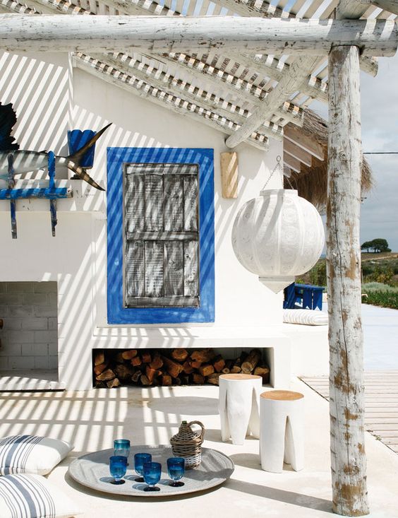 a bold white and blue beach patio with framed shutters, white furniture, striped textiles, a paper lamp and blue accessories
