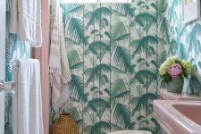 a bright tropical bathroom with tropical wallpaper, a pink sink and toilet, neutral linens