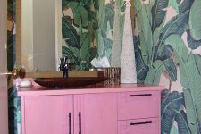a bright tropical powder room with banan leaf wallpaper, a hot pink vanity, a statement mirror and a vintage chandelier