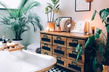 a catchy attic tropical bathroom with a vintage storage unit, a copper clawfoot tub, potted plants and candles plus copper touches