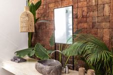 a catchy tropical bathroom with a brick wall, a stone vanity, a stone sink, a woven lamp and a basket