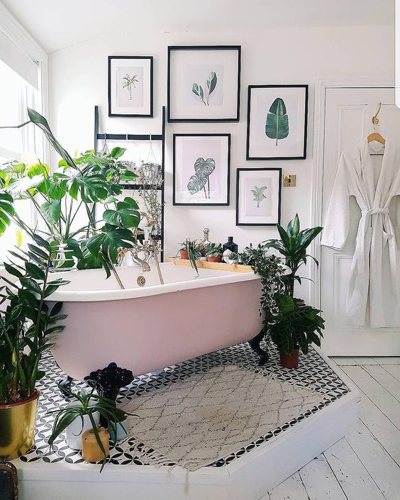 a catchy tropical bathroom with a pink clawfoot tub on a platform, a tropical gallery wall, potted plants and mosaic tiles
