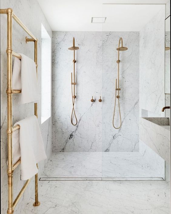 a chic and elegant bathroom done in white marble and gold hardware plus a floating sink and vanity