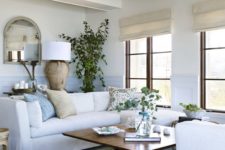 a chic coastal living room with touches of blue and light blue, creamy furniture and tan items plus a dirftwood lamp