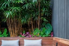 a chic modern outdoor fire pit with a built-in wooden bench with pillows, an ethanol fire bowl with white pebbles