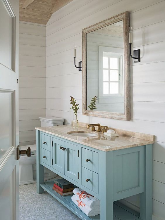 a coastal-inspired bathroom with a light blue vanity, a framed mirror and cool tiled floor