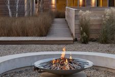 a contemporary fire pit of concrete, with pebbles on the ground and a metal fire bowl looks chic and very edgy