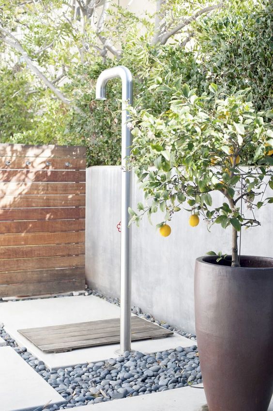 a contemporary outdoor shower done with pebbles, concrete and wood and potted lemons for an ambience