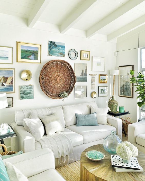 a cozy beach living room with white upholstered furniture, a large gallery walls with photos, artworks and a decorative basket