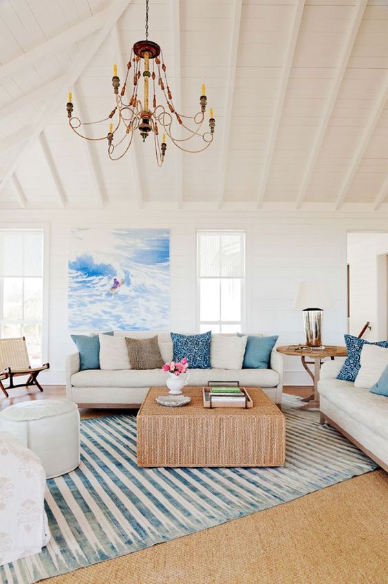 a cozy coastal living room with a cork coffee table, a striped rug, blue pillows and white furniture