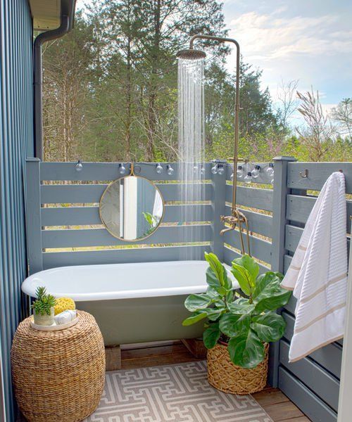 a cozy rustic-style bathroom hidden with screens, a bathtub in green and some wicker ottomans and planters