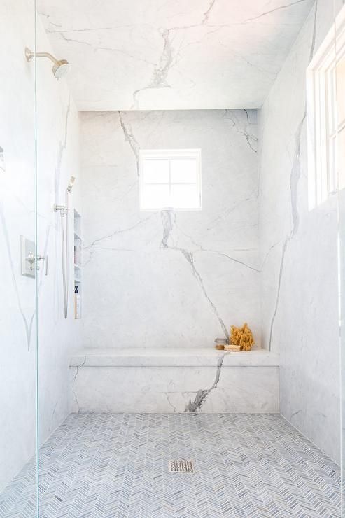 a fresh shower space with white marble and little herringbone clad tiles on the floor plus a window