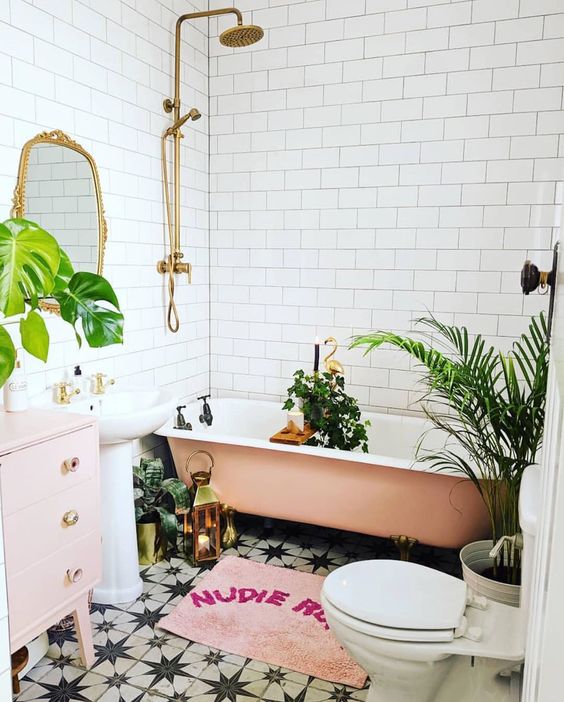 a glam tropical bathroom in neutrals, a pink tub, a pale pink vanity, a pink rug and potted plants, gold touches