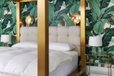 a glam tropical bedroom with a statement tropical print wall, a large gold framed bed and gilded sconces