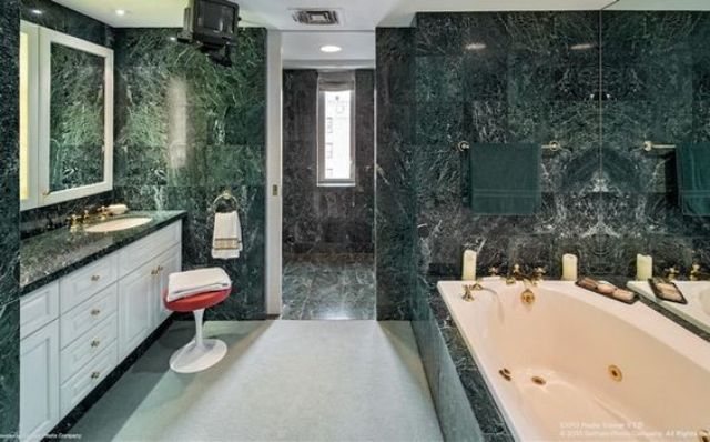 a large modern bathroom clad with green marble tiles is made fresher with white furniture and cabinets