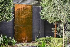 a lovely outdoor space with a copper waterfall, some greenery around, wooden stools and a metal fire bowl is amazing