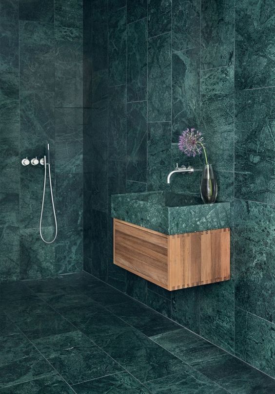 a minimalist bathroom fully covered with green marble tiles that are contrasting light colored wood