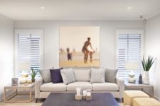 a modern beach living room in neutrals and navy, with printed piillows, jute square ottomans and an artwork