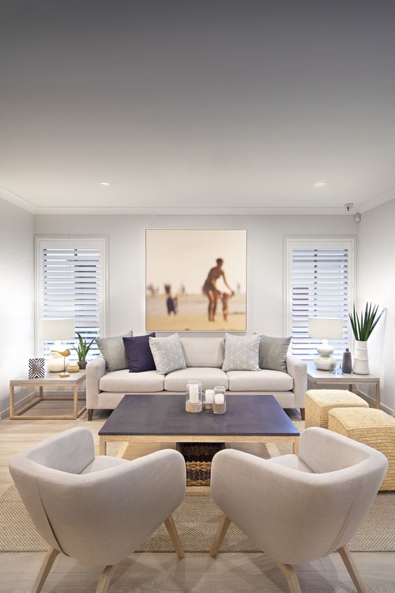 a modern beach living room in neutrals and navy, with printed piillows, jute square ottomans and an artwork