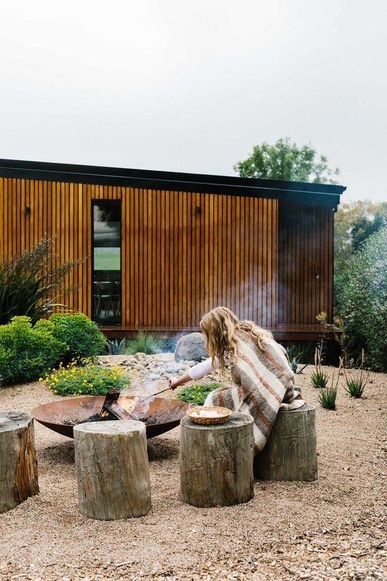 a modern outdoor space with greenery and blooms, with tree stump stools and a wrought iron fire bowl is amazing