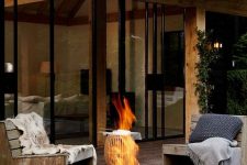 a modern outdoor space with simple wood and metal chairs with pillows, a black metal fire bowl that can be moved