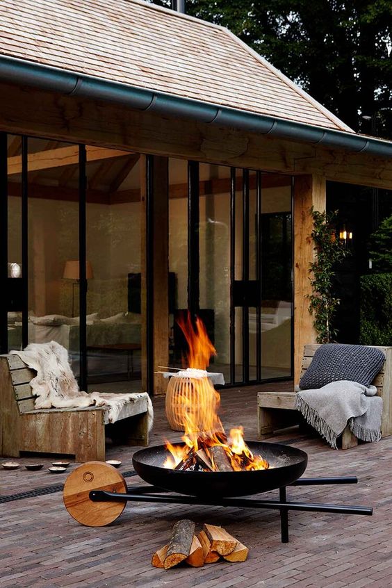 a modern outdoor space with simple wood and metal chairs with pillows, a black metal fire bowl that can be moved
