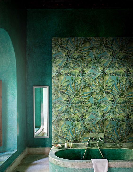 a moody tropical bathroom with a statement mural, a green plaster tub and grene plaster walls