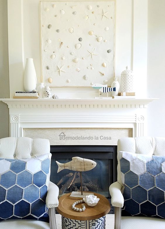a neutral seaside mantel with white vases, little figurines, a beachy artwork with seashells, pebbles and starfish