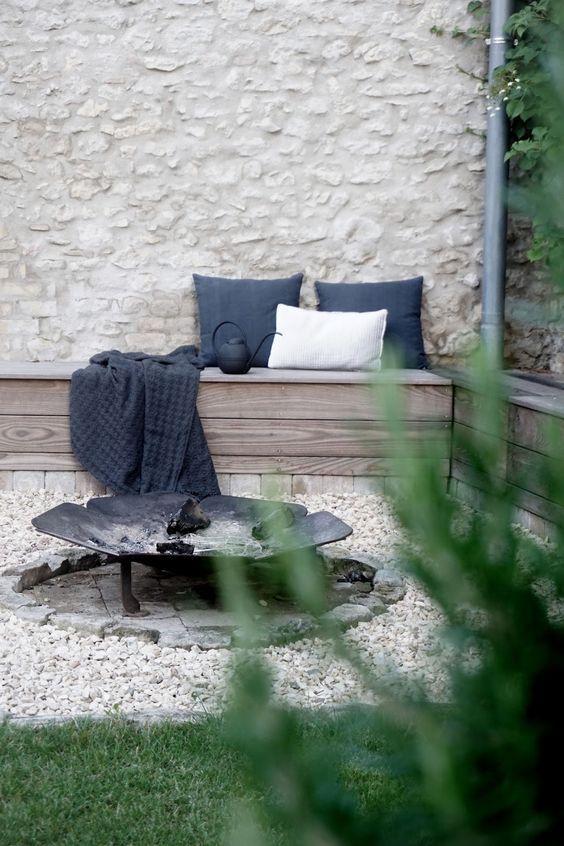 a relaxed outdoor space with a built-in corner bench with pillows, a wrought iron fire bowl on a brick spot is a lovely nook