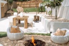 a relaxed white tropical outdoor space with a simple metal fire bowl and white chairs around it plus a dining space