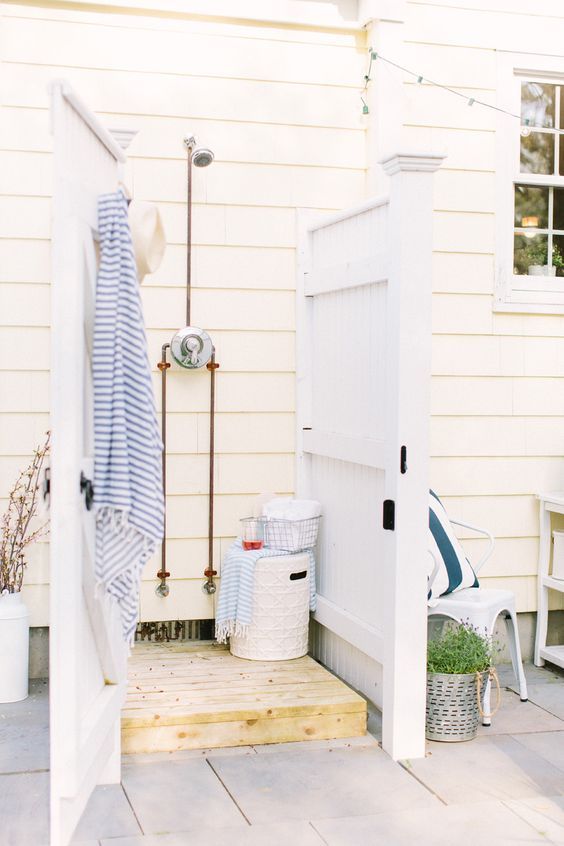 a seaside inspired outdoor shower with vintage white doors, wood and striped towels in blue