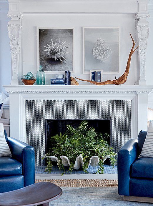 a seaside mantel with driftwood, blue books, a green bottle, glass floats in a bowl and black and white sea-themed artworks