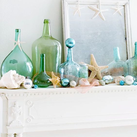 a seaside mantel with seashells, blue and pearl ornaments, blue and green bottles, starfish and beads is lovely